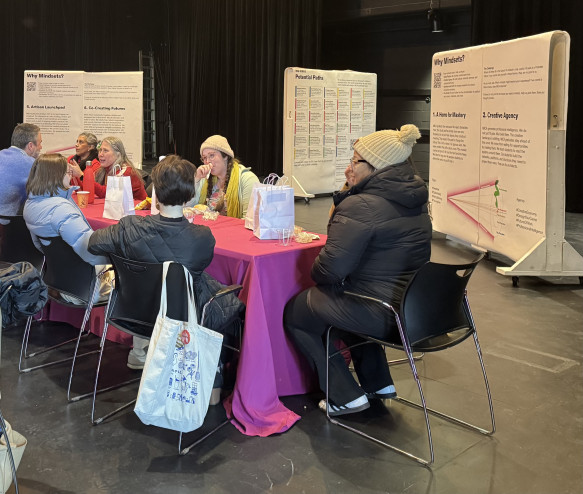 Several community members gather at the Strategic Planning engagement experience, seated at tables with large posters displayed behind them.