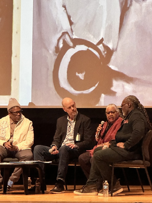 Leslie King Hammon, Dean Emerita speaking with microphone in front of image by Professor Raél Salley